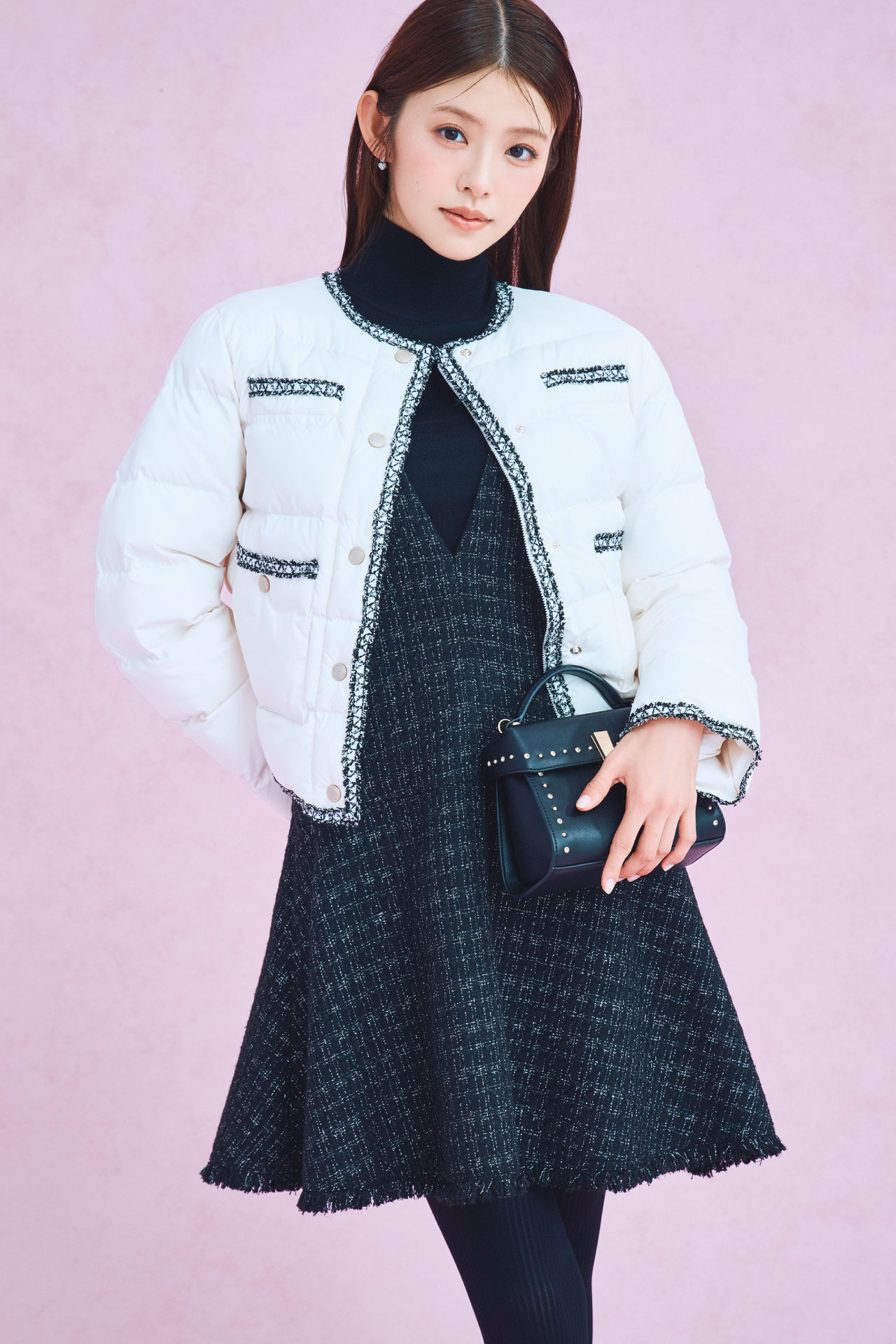 アイボリー色のトリムデザインキルティングジャケット、ブラック色のジャンスカセットアップとリュタンビジュースタッズポシェットを着用した女性のイメージ
