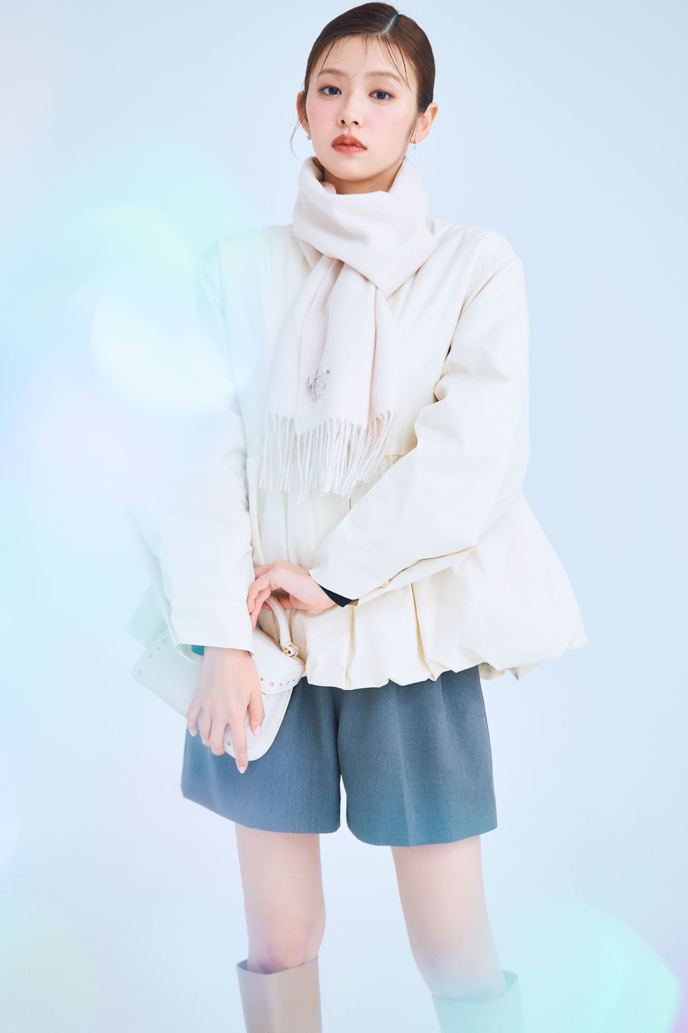 アイボリー色の薄中綿ペプラムノーカラーコートとビジューブローチ付きカシミヤ混ストール、バリエーションショートパンツ、リュタンビジュースタッズポシェット、ロゴメタル付きロングブーツを着用したモデル画像