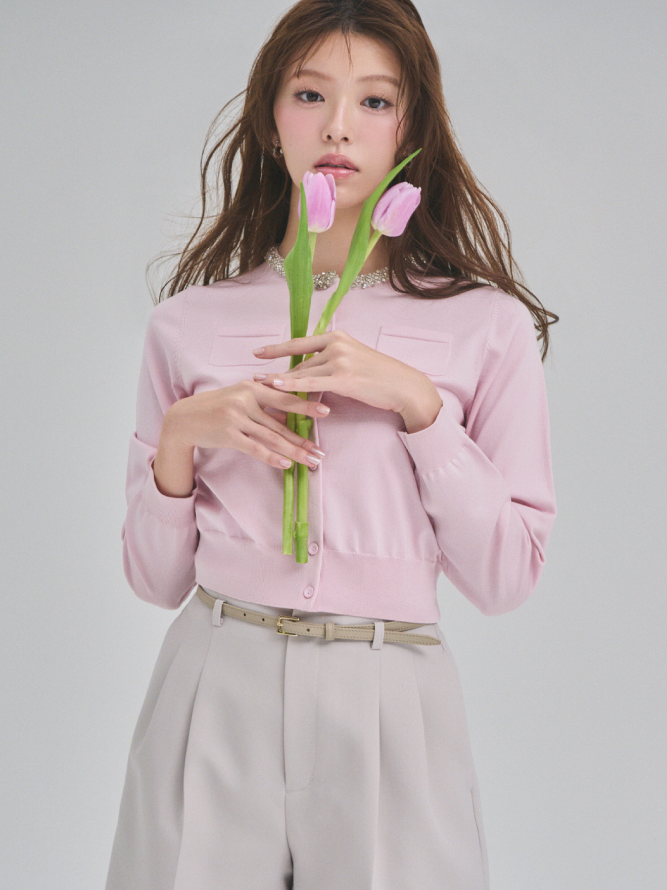 ピンク色のチューリップを持ち、シルクブレンドビジューネックカーディガン、ベルト付きショートパンツ、ハートビジューフープピアスを着用したモデル画像